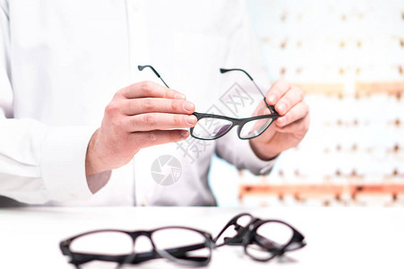 眼镜店里拿着眼镜的配镜师有镜片的眼科医生白色外套的专业验光师有许多镜片的店内修复或比较眼镜背景图片