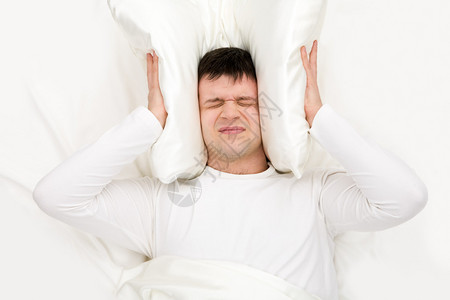 男人失眠和用垫子捂住耳朵的形象图片