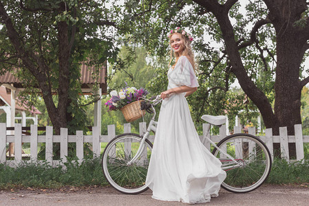 穿着花圈和结婚礼服的年轻新娘站着脚踏自行车图片
