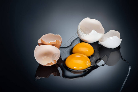黑色背景中带有蛋黄蛋白质和蛋壳的生碎鸡蛋图片
