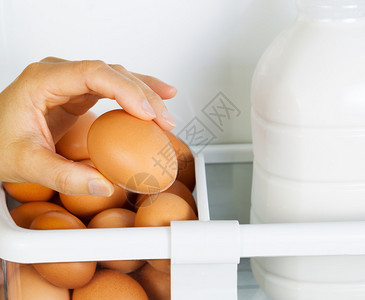 女手在冰箱门架内选择含部分牛奶容器的新鲜褐色有机蛋的照片单位图片