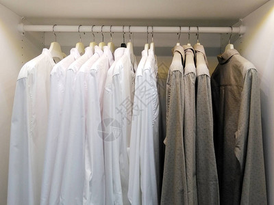 一排灰色和白色的衬衫挂在白色衣柜的衣架上图片