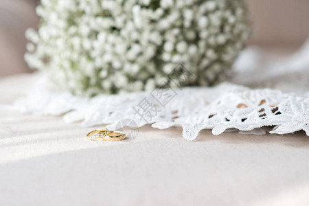 婚环和新娘花束在白带色的婚纱上有选择的焦图片