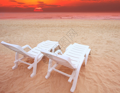 在海边沙滩和日落下的两把沙滩椅图片
