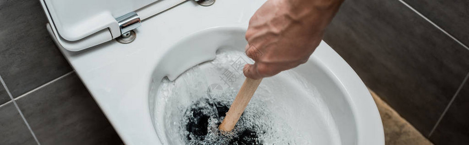 在现代卫生间用灰色瓷砖冲洗时使用马桶中的柱塞的水管工的裁剪视图片