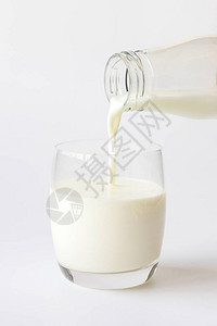 玻璃瓶将牛奶倒入白色背景的玻璃杯中图片