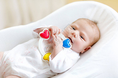 可爱的健康新生婴儿玩五颜六色的拨浪鼓玩具在家里的白色床上新出生的孩子图片