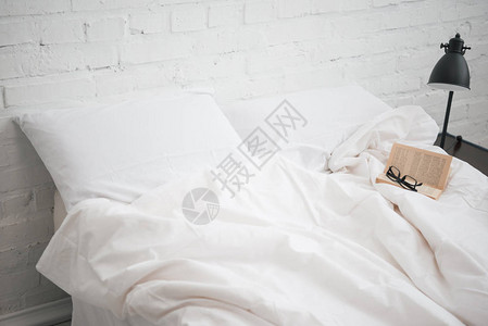 床上的眼镜和书白色的毯子和枕头灯图片