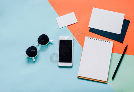 现代彩色背景中带智能手机空白信封太阳镜和空白笔记本的创意图片