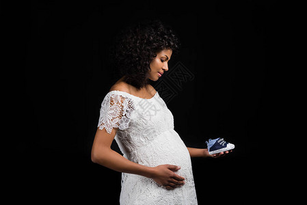 孕妇触摸肚子并手握一双小鞋子的侧面视角图片