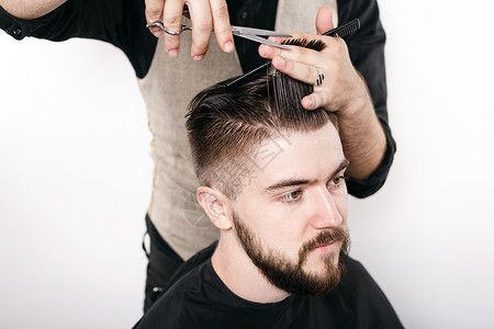 理发师用剪刀和黑梳子剪头发在英俊的满意客户的皇冠上用白色背景图片