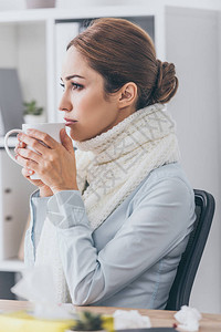 穿着围巾在办公室喝热茶的生病女图片