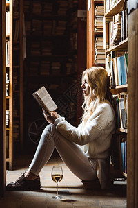 金发女人看书和坐在图书馆的地板图片