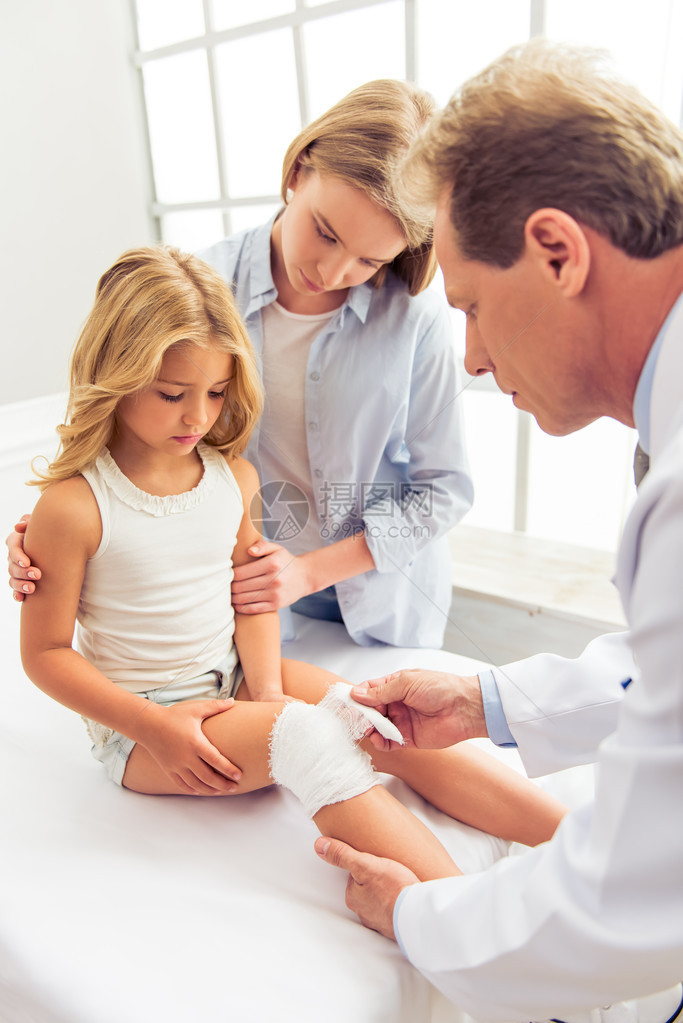 年轻中年儿科医生给小女孩的膝盖贴了绷带图片