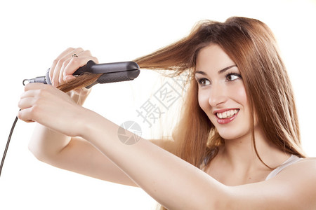 微笑的红发女孩使用直发器拉直头发图片