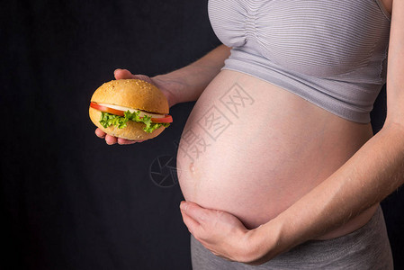 一个有肚子的孕妇拿着一个汉堡怀孕期间快餐和不健图片