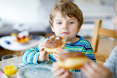 可爱的小男生在室内吃甜圈家庭厨房或学校食堂的金发孩子可爱的孩子和图片