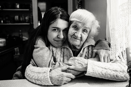 和一位成年孙女在村舍的拥抱中的老年妇女黑白相片图片