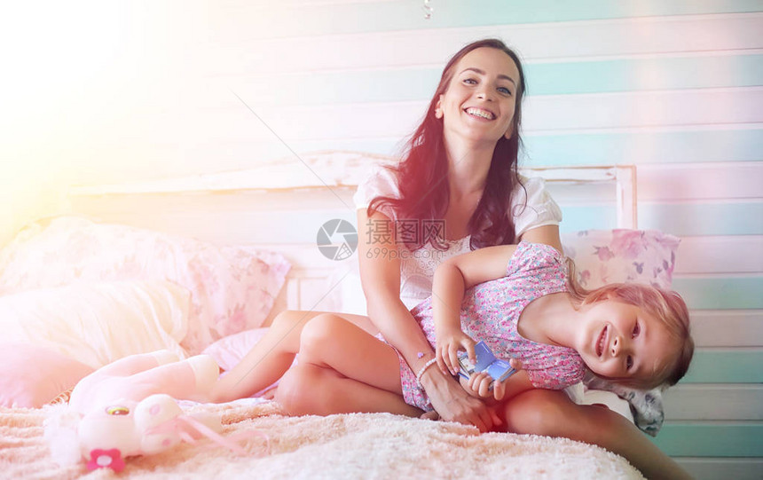 年轻的女孩读一本书带着女儿的年轻女孩正坐在床上花园旁村图片