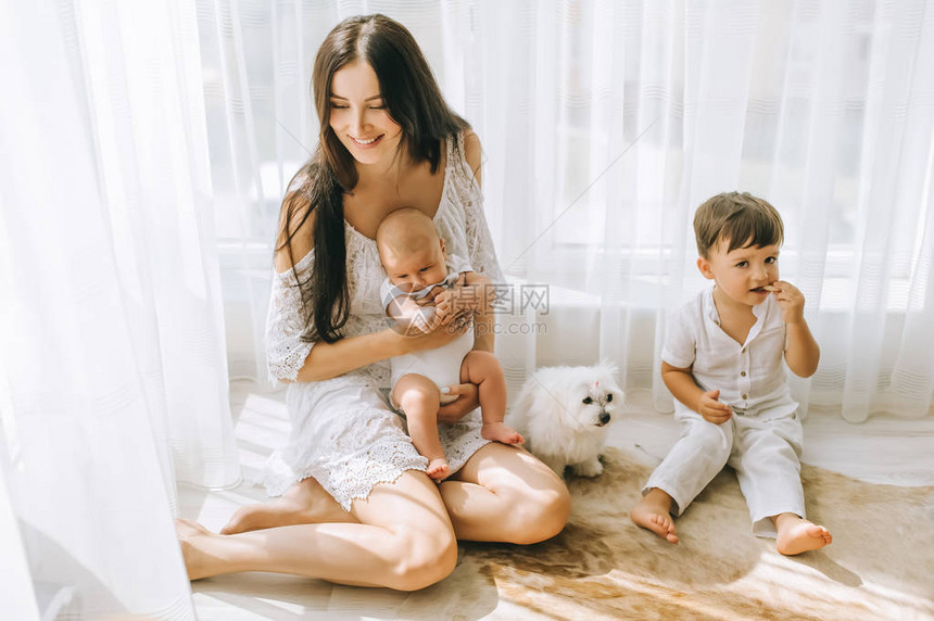 坐在地板上与孩子和比琴狗一起坐在一起的年轻快乐母亲图片