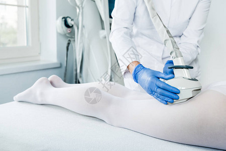 在仪器美容诊所的腿部有乳液喷脂手术的妇女图片