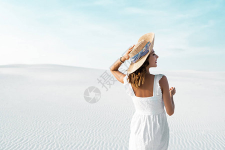 穿着白裙子和草帽的美丽女孩背面景色蓝天空沙图片