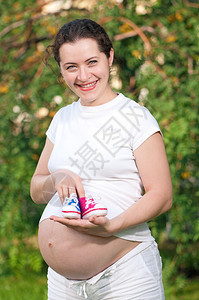 孕妇在户外公园里抱着不同颜色的婴儿短靴图片