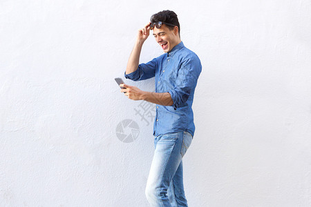 一个快乐的年轻男子走路和在手机上阅读短图片