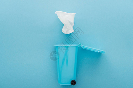 白色折叠塑料杯倒在玩具垃圾桶底蓝色背景背景图片