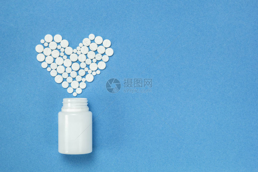 以心脏形式呈现的白色平板块蓝色背景上装着瓶子的药丸图片
