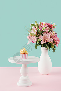 蛋糕架上的一个纸杯蛋糕和花瓶里的一束百合花图片