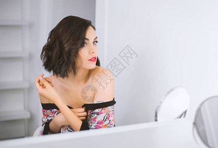 年轻迷人的黑发模特穿着浴袍坐在镜子前图片