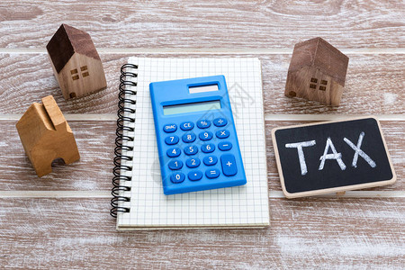 地产税概念与计算器和房屋模型及木制桌背景