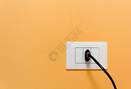 黑色插头入橙色内墙上的墙壁插座中图片