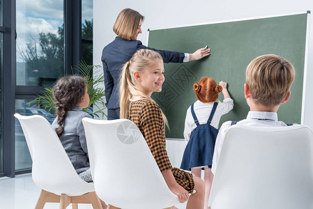 年轻女教师有小学生站在黑板上解释课文背景图片