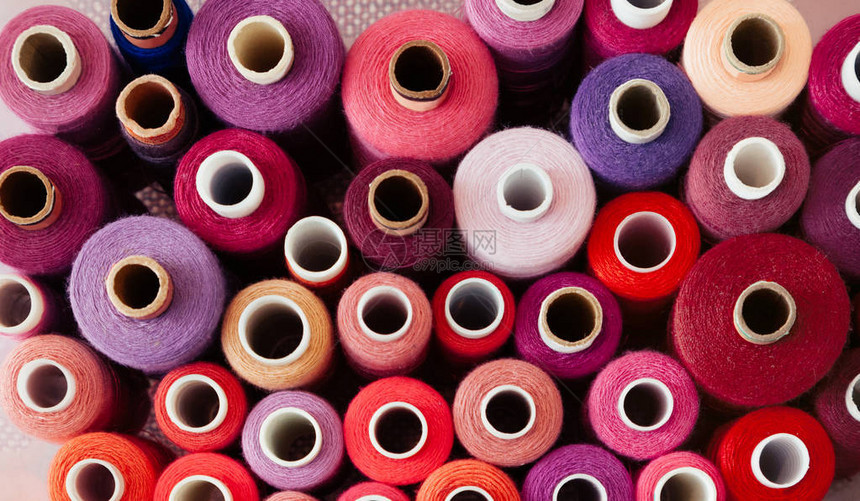 粉红色背景上的一组不同颜色的线程许多用于缝纫和针线活的线在颜色和尺寸上都不同多彩姿图片