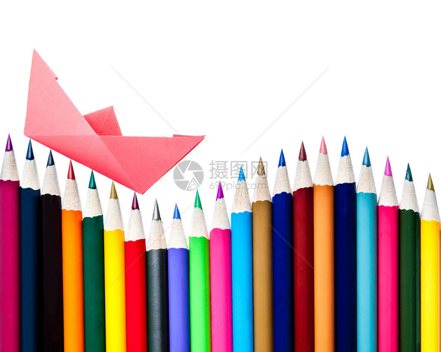 一艘纸船漂浮在一排彩色铅笔上白色与图片