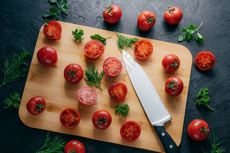 烤熟的西红柿在切肉板上被切成绿菜利刃和深色背景隔绝背景