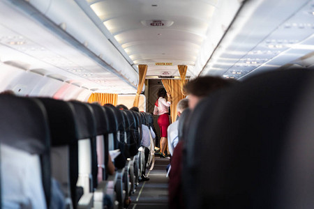 商业乘客飞机上身穿红色制服的空姐无法辨认的乘客坐在座图片