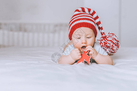 穿着红帽和白条纹帽子的婴儿在床上与图片