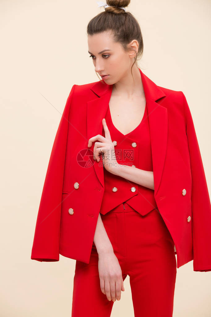 穿着红色燕尾服的吸引人时装模特在演播室上摆着夹克在她肩膀上穿三件西装和马尾辫的图片