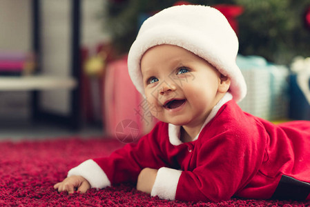穿着圣诞套装的快乐小婴儿躺在红地毯上图片