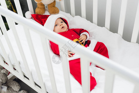 高角度的视觉可爱的小婴儿在圣塔西服躺在婴儿床与泰图片