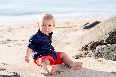 一个岁的小男孩坐在沙滩上直接看着摄图片