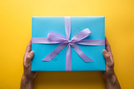 黄色背景带紫色彩带的蓝色礼品盒男图片