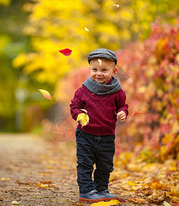 戴着帽子围巾和毛衣的快乐小男孩站在公园里图片