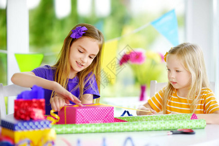 两个可爱的小姐妹用五颜六色的包装纸包装礼物可爱的兄弟姐妹在家图片