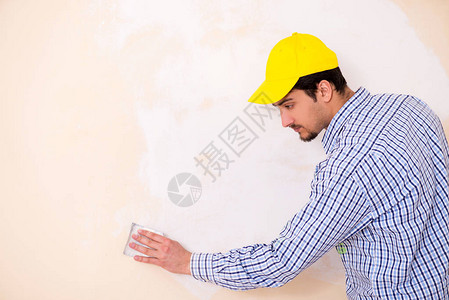 年轻承包商用砂纸打磨墙壁背景图片