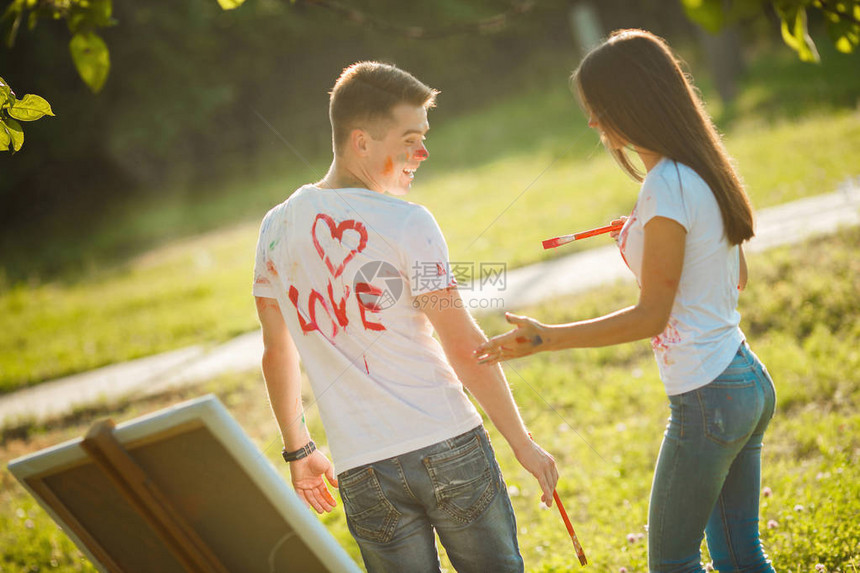 漂亮的夫妇在户外露天玩得开心年轻男女用彩色颜料在彼此的T恤上用刷子在大自然的图片