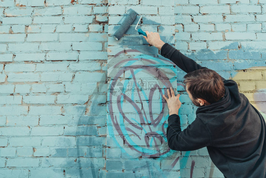 男街头艺术家用滚筒在墙上画彩色涂鸦图片